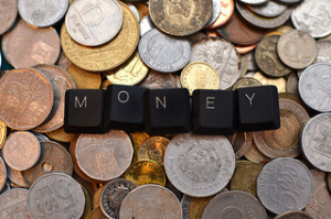 Keyboard keys spelling out 'money' sitting on top of a lot of coins