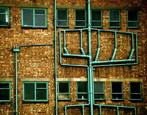 Drainage pipes running down the wall of a factory, branching and merging as they descend, similar to the disorganisation that branches can cause in Git and Mercurial.