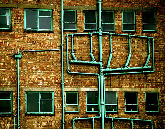 Drainage pipes running down the wall of a factory, branching and merging as they descend.