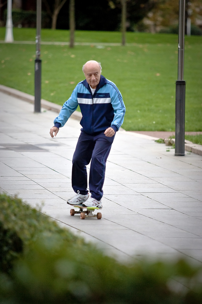 An elderly man riding a skateboard in a tracksuit and looking very focused