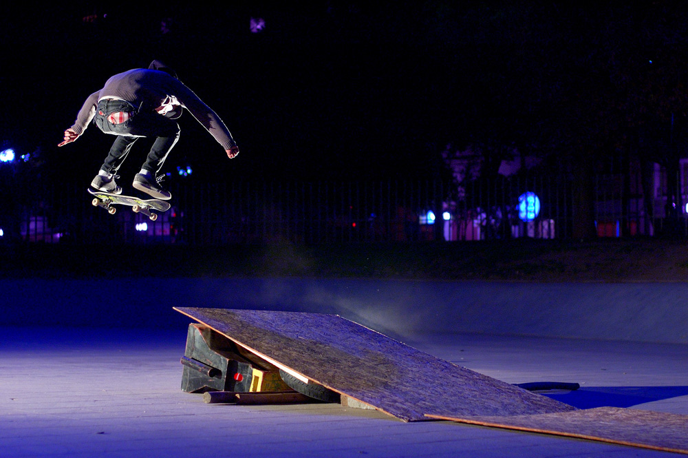 A skateboarder jumping off a wooden ramp at night