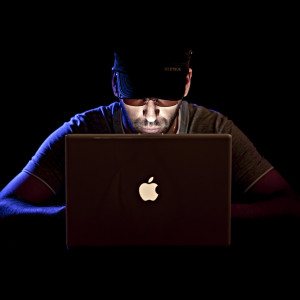 Hacker-looking character sitting at a Mac in a dark room, checking out your microservices security