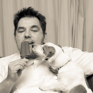 A man licking an ice cream while a dog tries to lick it as well. Reminiscent of the kind of undesirable coupling created by shared libraries in microservices