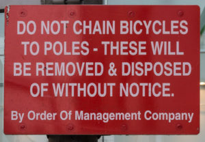 Ambiguous sign reading "Do not chain bicycles to poles - these will be removed & disposed of without notice"